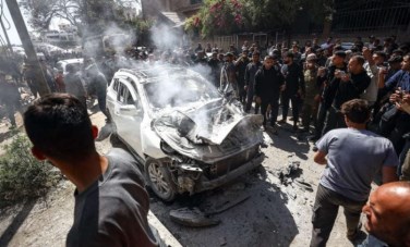مواطنون يتجمعون قرب سيارة مدنية استهدفتها غارة إسرائيلية بمدينة غزة